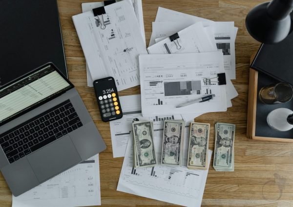 Overhead view of financial documents, cash, and technology on a wooden desk.